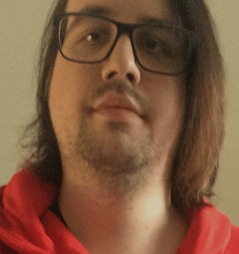 Selfie von Romy, einer weißen Person mit braunen schulterlangen Haaren, Bart und Brille